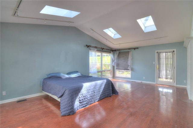 bedroom featuring rail lighting, baseboards, wood finished floors, visible vents, and lofted ceiling with skylight