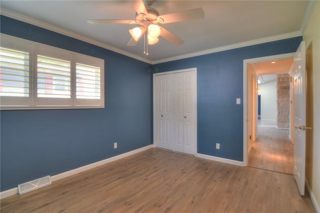 unfurnished bedroom featuring visible vents, crown molding, wood finished floors, baseboards, and a closet