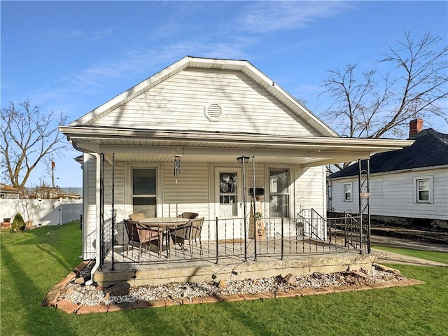 rear view of property with covered porch, a lawn, a gambrel roof, and fence