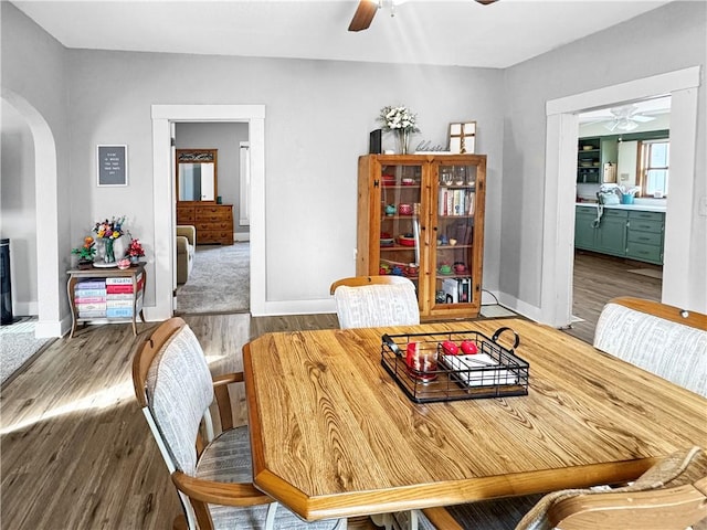 dining room with a ceiling fan, arched walkways, baseboards, and wood finished floors