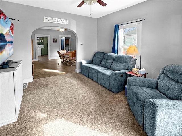 living area featuring a ceiling fan, arched walkways, baseboards, and carpet