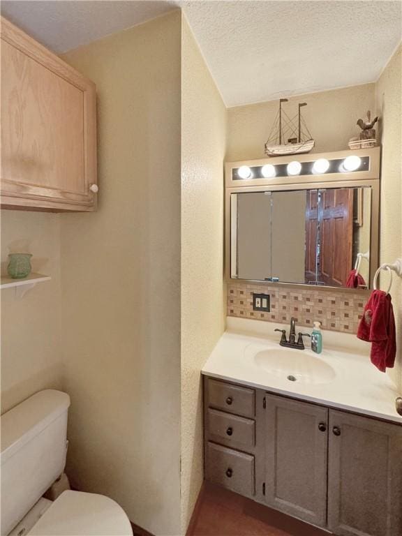 half bath with a textured ceiling, vanity, backsplash, and toilet