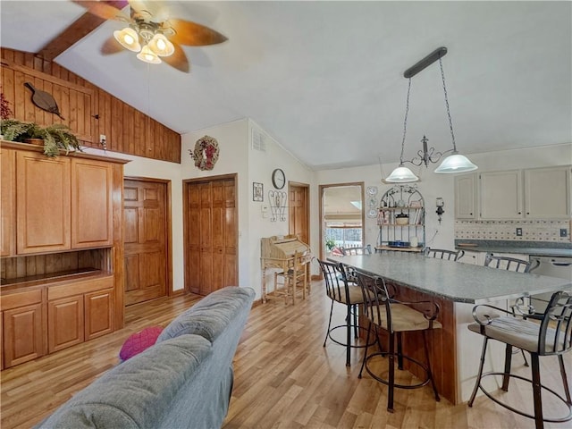 kitchen with light wood finished floors, decorative backsplash, decorative light fixtures, vaulted ceiling with beams, and a kitchen bar