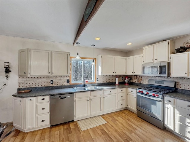 kitchen featuring light wood-type flooring, dark countertops, stainless steel appliances, and a sink