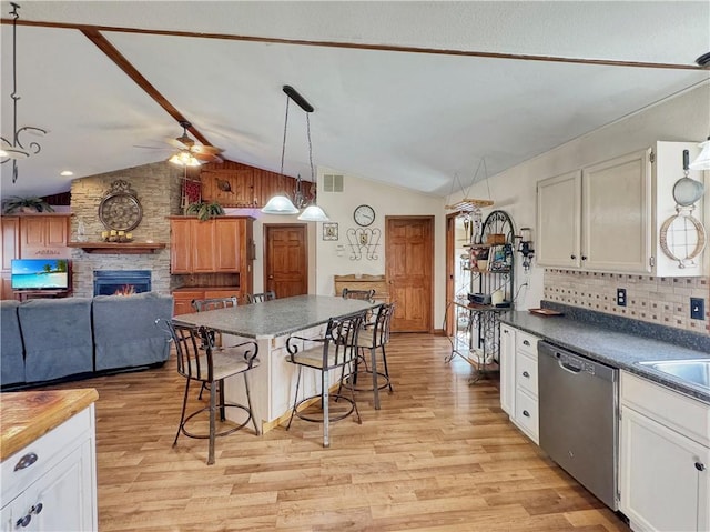 kitchen featuring light wood-type flooring, vaulted ceiling, dishwasher, and a stone fireplace