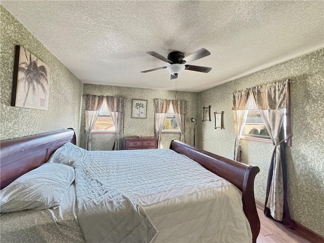 bedroom with a textured ceiling, ceiling fan, wood finished floors, and wallpapered walls