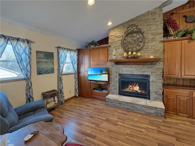 living room featuring light wood-type flooring, lofted ceiling, a stone fireplace, and recessed lighting