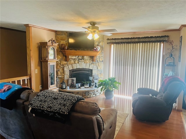 living room with a stone fireplace, crown molding, ceiling fan, a textured ceiling, and wood-type flooring