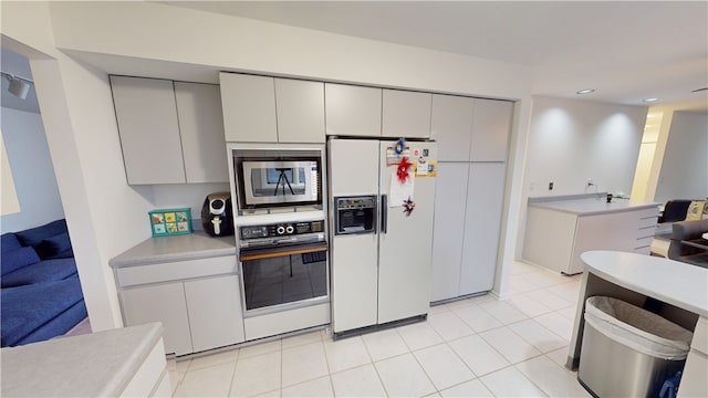 kitchen featuring light tile patterned floors, oven, white refrigerator with ice dispenser, light countertops, and stainless steel microwave