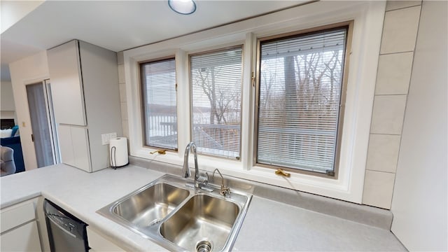 kitchen with white cabinets, light countertops, a sink, and stainless steel dishwasher