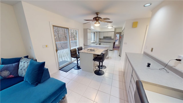 interior space with light tile patterned floors, a ceiling fan, under cabinet range hood, a kitchen bar, and recessed lighting