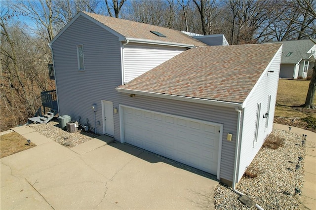 view of home's exterior featuring driveway, central air condition unit, a garage, and roof with shingles