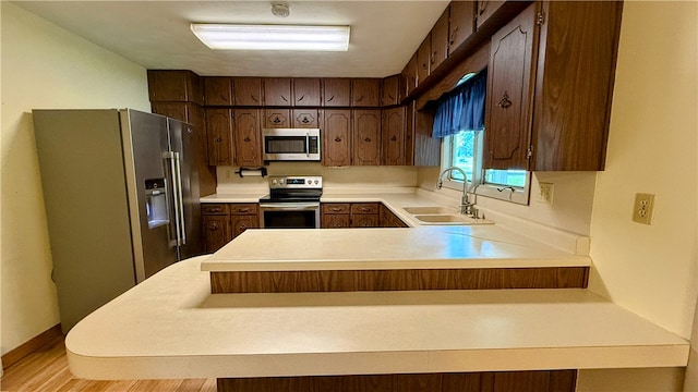 kitchen with dark brown cabinetry, sink, kitchen peninsula, appliances with stainless steel finishes, and light wood-type flooring