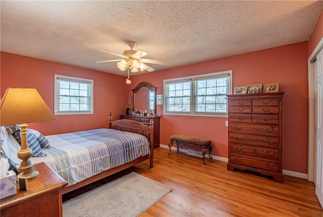 bedroom featuring multiple windows, baseboards, light wood finished floors, and a textured ceiling