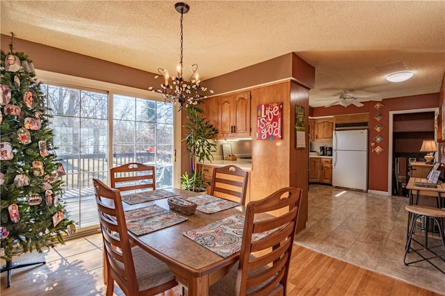 dining area with a textured ceiling, light wood-style flooring, and ceiling fan with notable chandelier