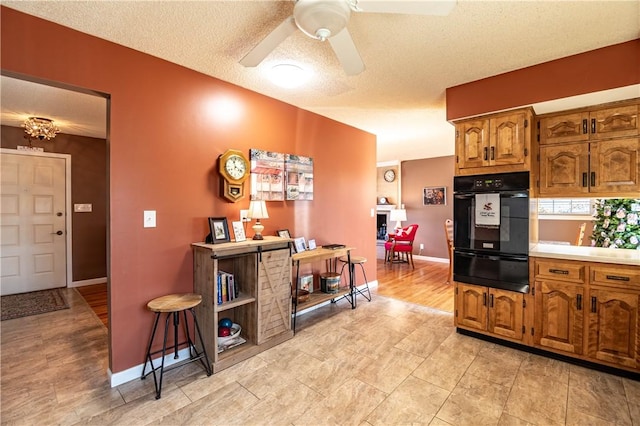 kitchen with ceiling fan, light countertops, brown cabinets, a textured ceiling, and a warming drawer