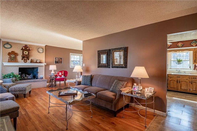 living area featuring light wood finished floors, a brick fireplace, a textured ceiling, and baseboards