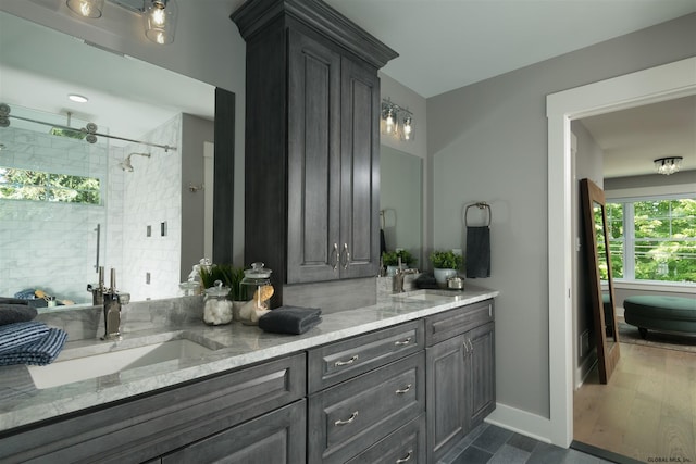 bathroom featuring dual sinks, hardwood / wood-style floors, a tile shower, and vanity with extensive cabinet space