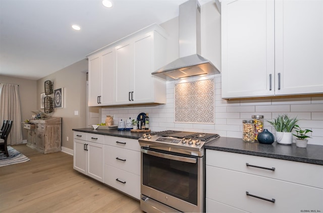 kitchen featuring backsplash, light hardwood / wood-style floors, white cabinets, stainless steel gas stove, and wall chimney range hood