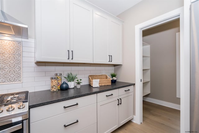 kitchen with backsplash, gas range, light wood-type flooring, white cabinets, and wall chimney range hood