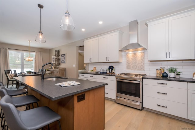 kitchen featuring white cabinetry, gas range, backsplash, wall chimney range hood, and sink