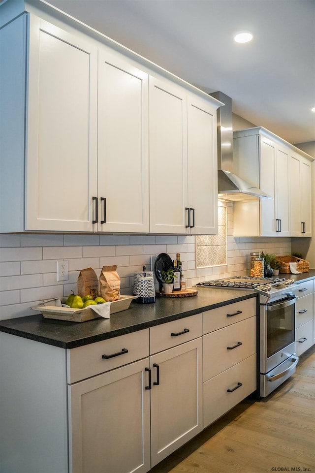 kitchen featuring white cabinets, light hardwood / wood-style floors, wall chimney exhaust hood, tasteful backsplash, and stainless steel range with gas cooktop