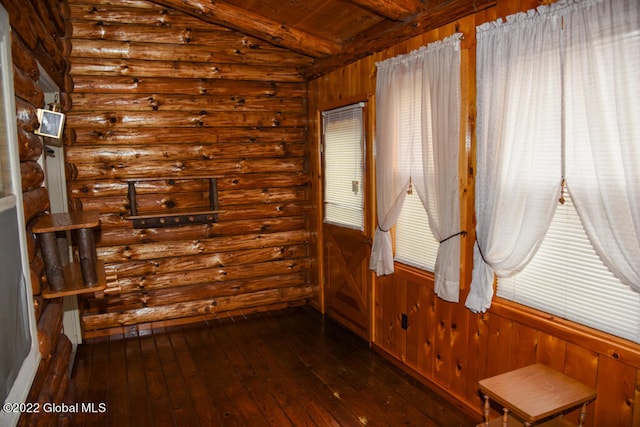 spare room with beam ceiling, rustic walls, and dark wood-type flooring