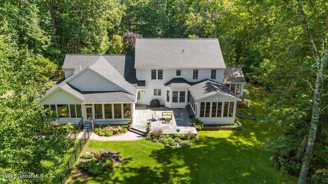 rear view of property featuring a sunroom, a shingled roof, and a lawn