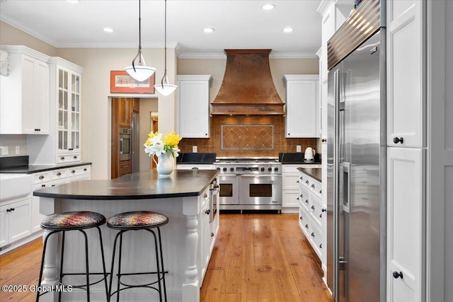 kitchen featuring dark countertops, high quality appliances, white cabinetry, and premium range hood