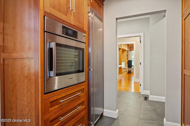 kitchen featuring baseboards, dark tile patterned flooring, brown cabinetry, and high end fridge