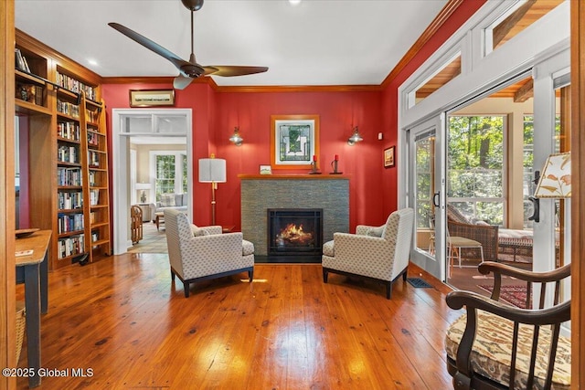 living area featuring hardwood / wood-style floors, ornamental molding, a lit fireplace, visible vents, and ceiling fan