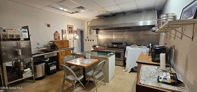 kitchen with wall chimney exhaust hood, a drop ceiling, a kitchen island, and gas range