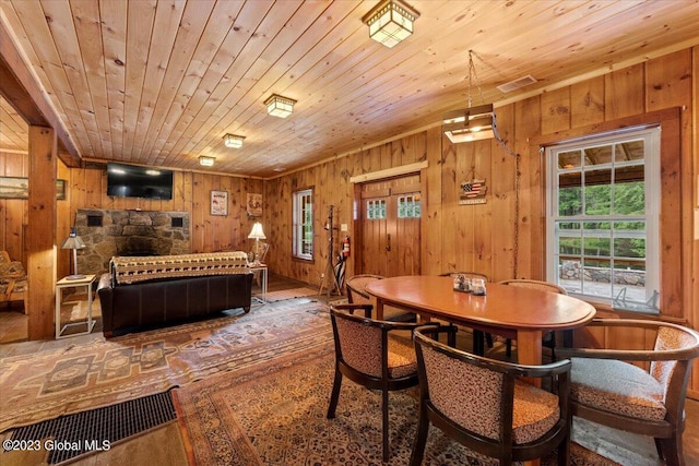 dining space featuring wooden ceiling, wood walls, dark wood-type flooring, and a stone fireplace