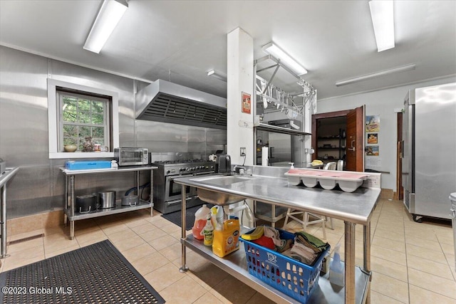 kitchen featuring appliances with stainless steel finishes, light tile floors, stainless steel counters, wall chimney exhaust hood, and sink