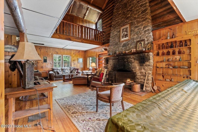 living room with high vaulted ceiling, wooden walls, a stone fireplace, and light wood-type flooring