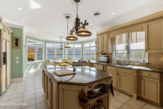 kitchen featuring dark stone counters, hanging light fixtures, tasteful backsplash, and a center island with sink