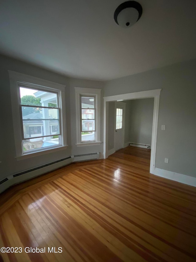 empty room with a baseboard radiator, plenty of natural light, and hardwood / wood-style flooring