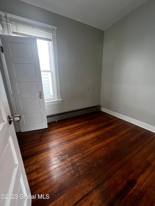 empty room featuring a baseboard heating unit and dark hardwood / wood-style flooring