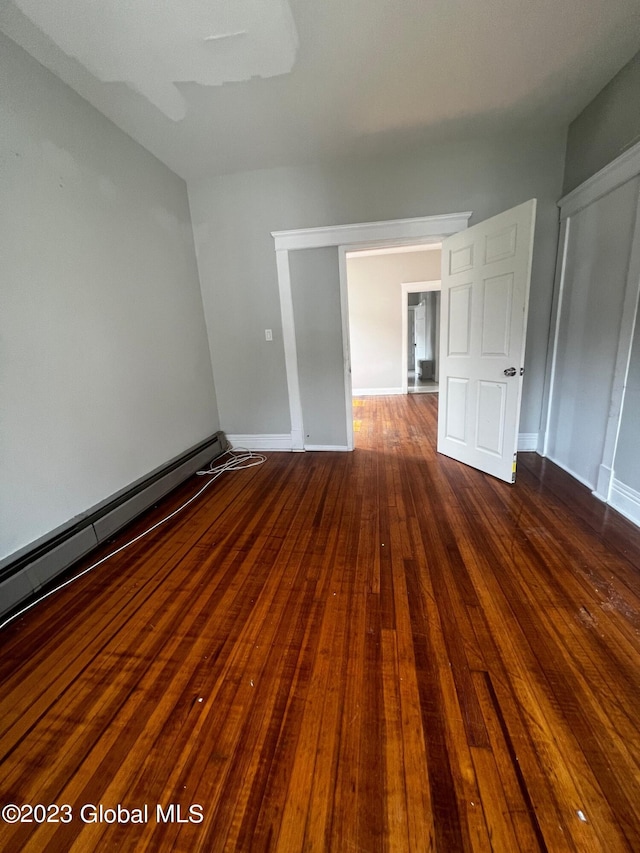 unfurnished room featuring dark hardwood / wood-style floors and a baseboard heating unit