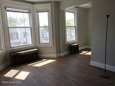 unfurnished room featuring dark wood-type flooring and radiator heating unit