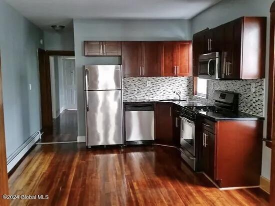 kitchen featuring decorative backsplash, a baseboard heating unit, appliances with stainless steel finishes, and dark hardwood / wood-style floors