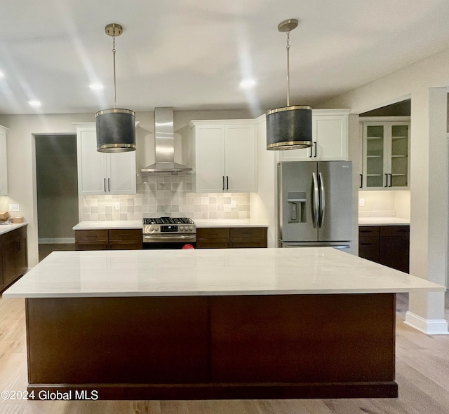 kitchen with wall chimney exhaust hood, appliances with stainless steel finishes, decorative light fixtures, and a kitchen island