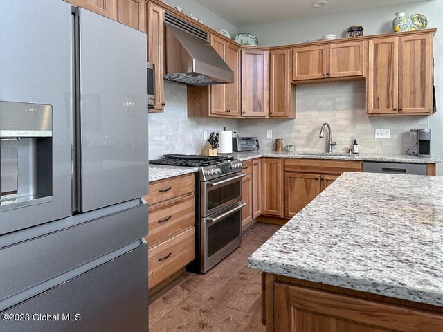 kitchen with hardwood / wood-style floors, stainless steel appliances, tasteful backsplash, and wall chimney exhaust hood