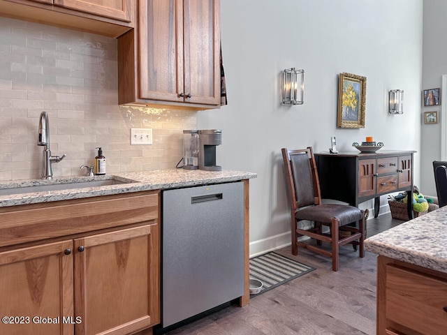 kitchen featuring hardwood / wood-style flooring, sink, dishwasher, light stone counters, and backsplash