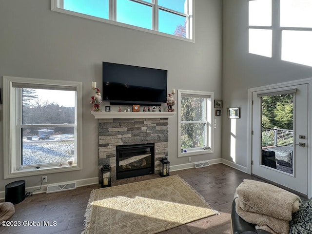 living room with hardwood / wood-style flooring, a healthy amount of sunlight, a towering ceiling, and a fireplace