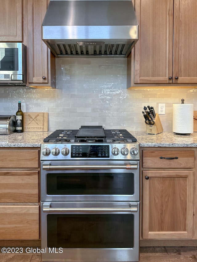 kitchen with appliances with stainless steel finishes, light stone countertops, tasteful backsplash, and wall chimney exhaust hood