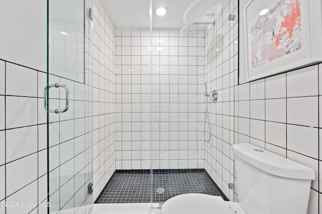 bathroom with toilet, tile walls, and a shower with shower door