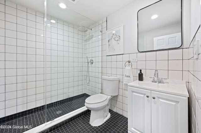 bathroom with vanity, tile patterned flooring, toilet, tiled shower, and tile walls