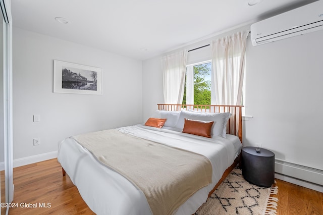 bedroom with light hardwood / wood-style floors, a baseboard radiator, and a wall mounted AC