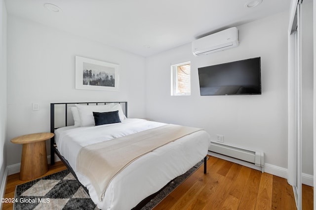 bedroom featuring a wall unit AC, hardwood / wood-style flooring, and baseboard heating